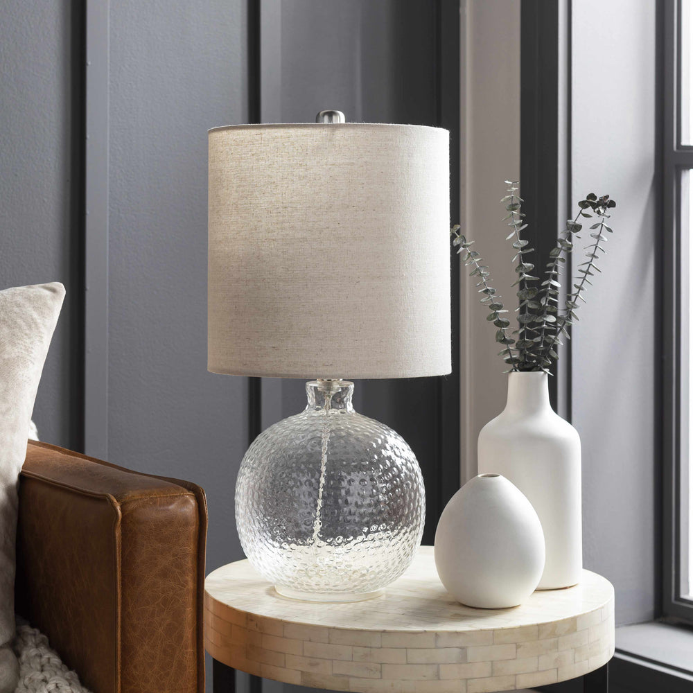 Decorative lamp with textured base on a side table next to a sofa.

Enetai Glass White Table Lamp