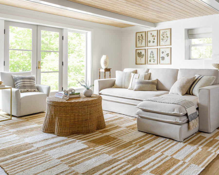 Modern living room with a beige sectional sofa, wicker coffee table, and decorative pillows.