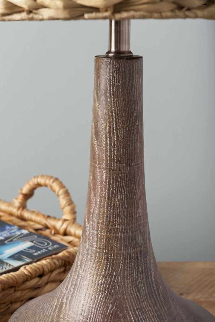 Close-up of a textured brown lamp base with a basket and books in the background.

Kabankalan Seagrass Resin Table Lamp